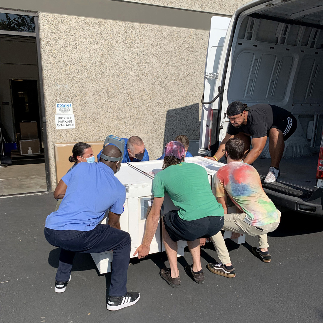 Photo of MSSS employees and the courier employee lifting the heavy container into the back of the shipping van.