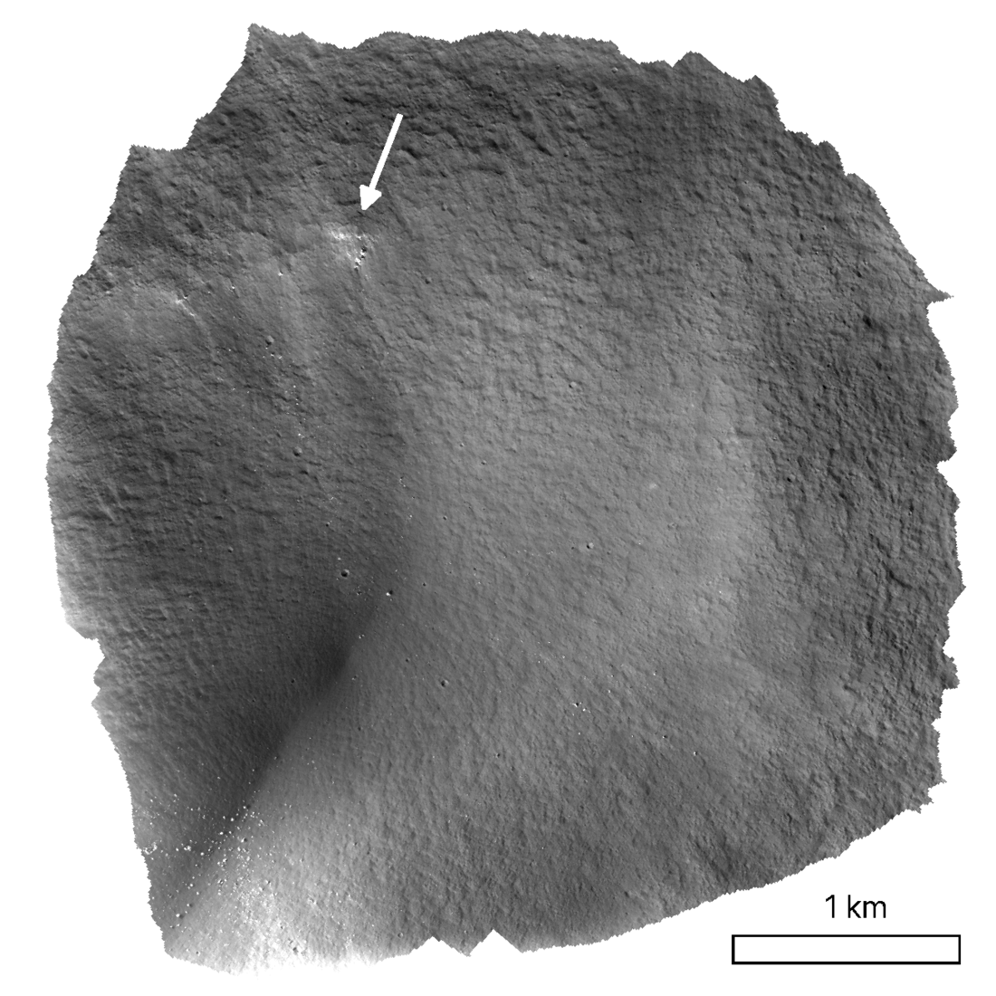 A roughly-circular portion of the volcanic vent in grayscale to display texture and depth. The lunar regolith slopes towards the center-bottom. In the upper-left region, a white arrow draws attention to a cluster of white spots that are distinct from the gray around them. A graphical scale is provided in the lower right measuring one kilometer. This portion of the vent is about four kilometers wide.